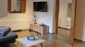 A modern living room with a sofa, a small table with a vase, a flat-screen TV, and a wooden cabinet. - Schrichten Apartment on the Edge of the Forest (Schmallenberg)