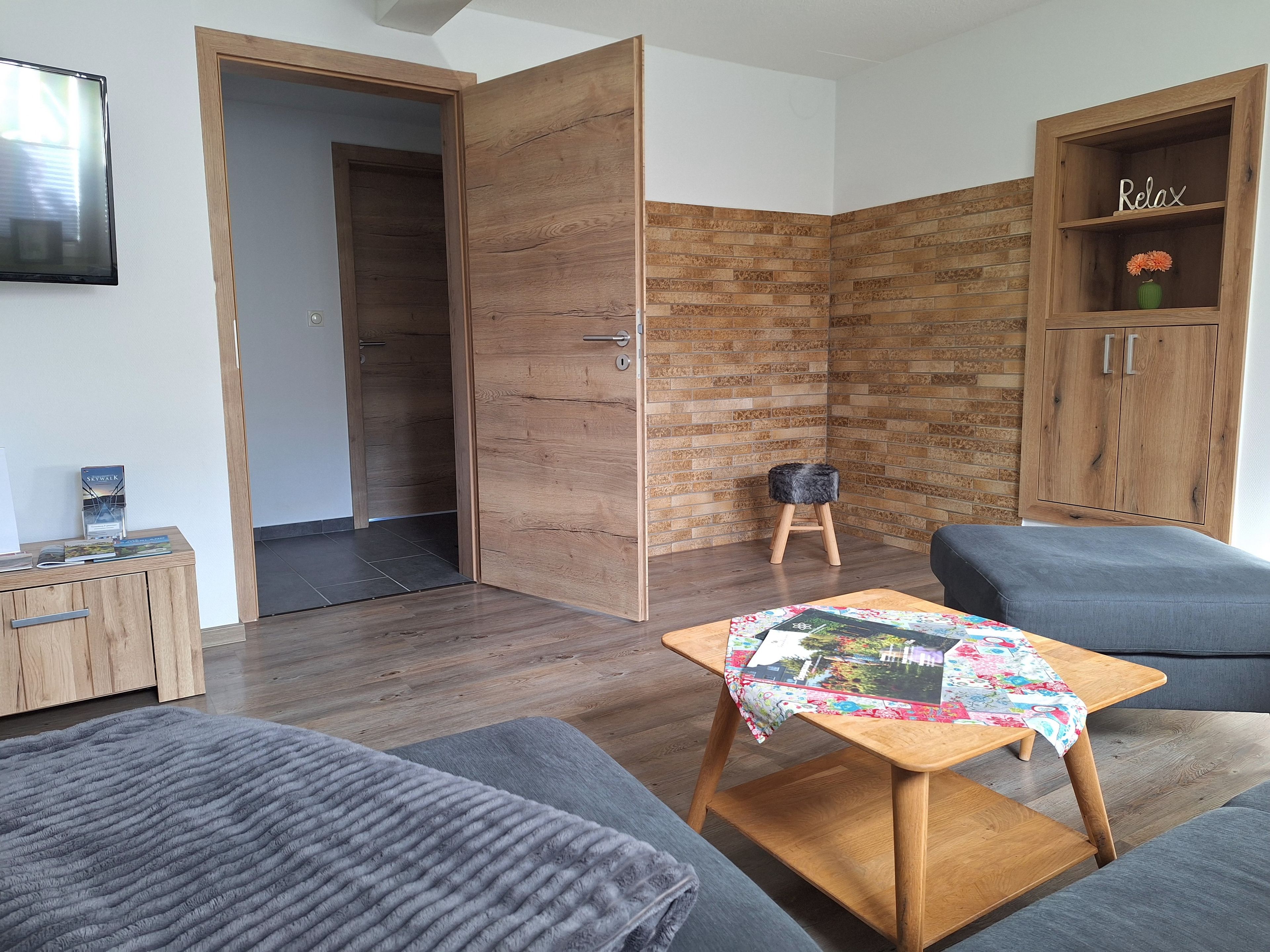 Een moderne woonkamer met een bank, een salontafel, een houten kastje met een 'Relax'-bordje en een klein krukje.