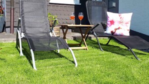 Two outdoor lounge chairs with cushions, a small table with two drinks, and a window with blinds. - Schrichten Apartment on the Edge of the Forest (Schmallenberg)