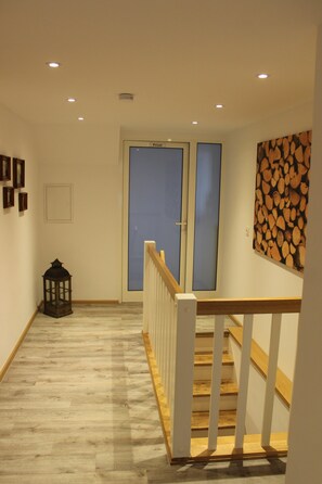 A hallway with a wooden floor, a staircase with white railings, a lantern, and a door with frosted glass panels. - Double Room on the Forest Edge with a View (Schmallenberg)