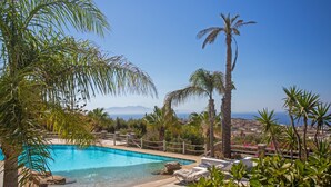 A swimming pool with stone flooring, surrounded by palm trees and a view of the sea. - Scorpios Dream By Bestofmikonos Country House with Private Pool, Wi-Fi & Air Conditioning (Mykonos)