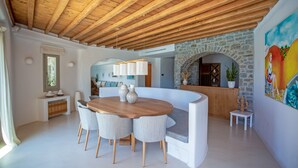 A modern interior with a wooden ceiling, a stone archway, a round wooden table with chairs, and a colorful mural. - Scorpios Dream By Bestofmikonos Country House with Private Pool, Wi-Fi & Air Conditioning (Mykonos)