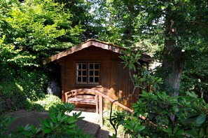 A wooden cabin with a window, surrounded by dense foliage. - Holiday Apartment Eichenwäldchen****, 129 sqm, 3 Bedrooms, Max. 8 Persons (Kirchhundem)