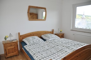 Una camera da letto con un letto in legno, un comodino con una lampada, uno specchio e una finestra che si affaccia su una chiesa.