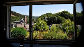 Une vue à travers une fenêtre sur une ville avec une église, entourée de verdure et de collines.