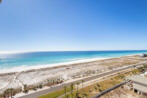 A coastal road with a beach and ocean view, a paved road, and sparse vegetation. - Stunning Sunset Views*Tower 5-1102 (Pensacola Beach)
