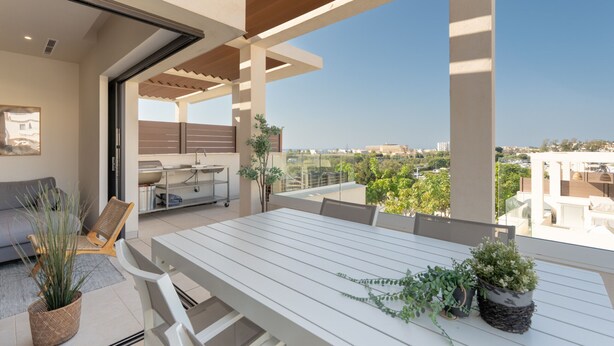 Un espacio exterior moderno para comer, con una mesa y sillas blancas, rodeado de plantas en macetas.