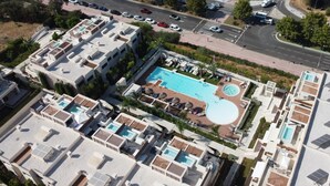 Vista aérea de un complejo residencial con varias piscinas, una carretera y coches aparcados.