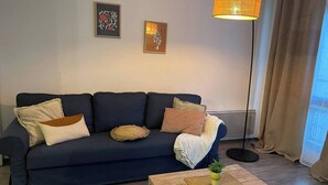 A living room with a dark blue sofa, a wooden coffee table, and a floor lamp. - Le rétro du Marché (La Rochelle)
