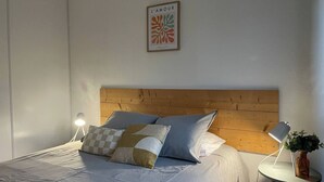 A neatly made bed with a wooden headboard, a bedside table with a lamp, and a framed artwork on the wall. - Le rétro du Marché (La Rochelle)