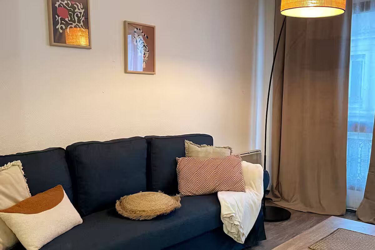 A dark-colored sofa with multiple cushions and a woven throw, positioned against a wall with two framed artworks.