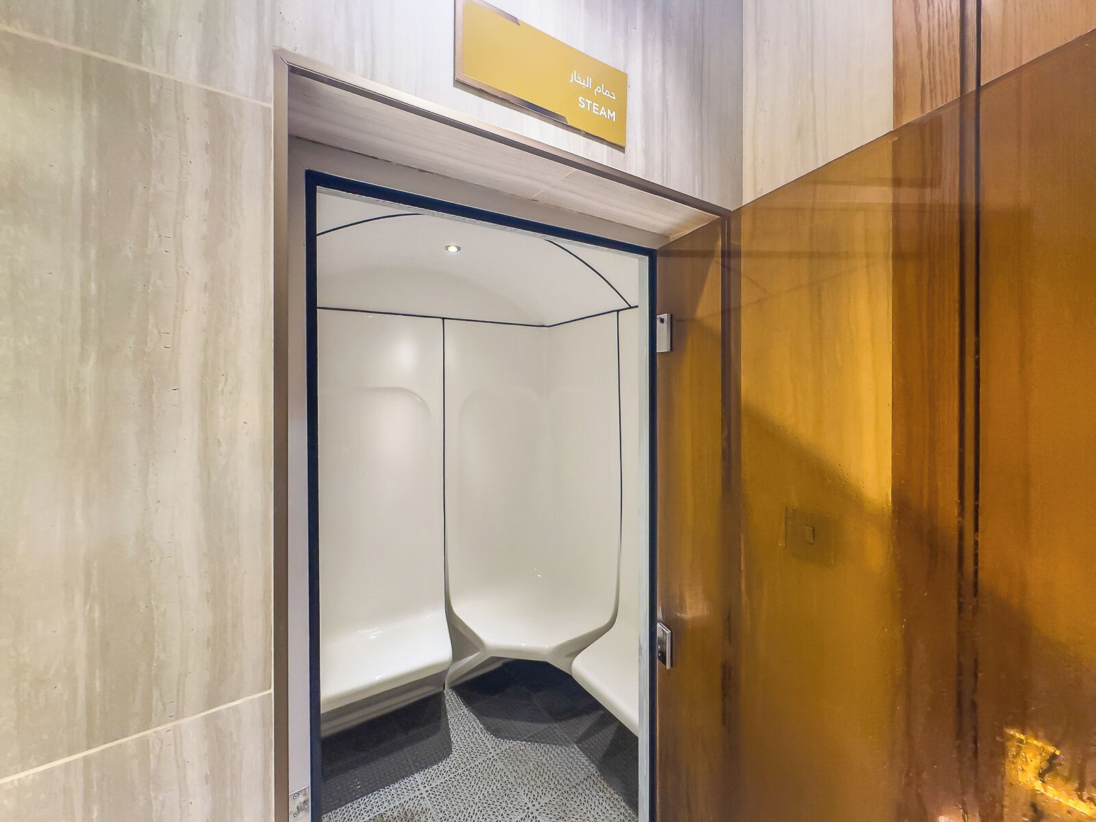 A modern elevator with a clear glass door and a sign indicating it is a steam room.