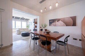 Un espace repas moderne avec une table en bois, quatre chaises et des luminaires suspendus. Un grand tableau abstrait orne le mur, et une plante est posée sur la table.