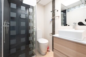 Une salle de bain moderne avec une douche à parois de verre, des toilettes blanches et un grand miroir au-dessus d’un lavabo.