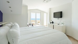 Camera d'albergo con un letto grande, una televisione montata a parete e vista mare dalle porte del balcone.