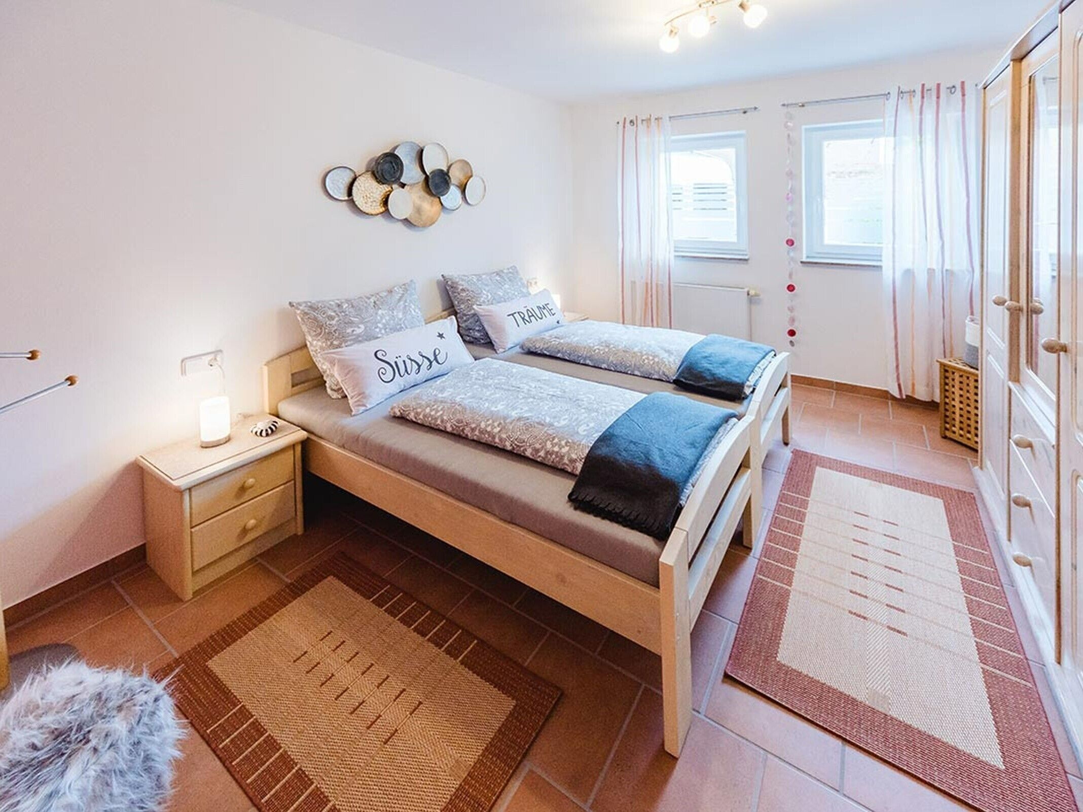 A double bed with two pillows, a bedside table with a lamp, a rug, and a wardrobe.