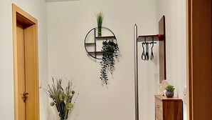 Un corridoio con una porta in legno, un tavolo rotondo con un vaso, una pianta sospesa, uno specchio e un appendiabiti.