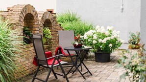 Un patio con un muro in mattoni, un tavolo con sedie e piante in vaso.