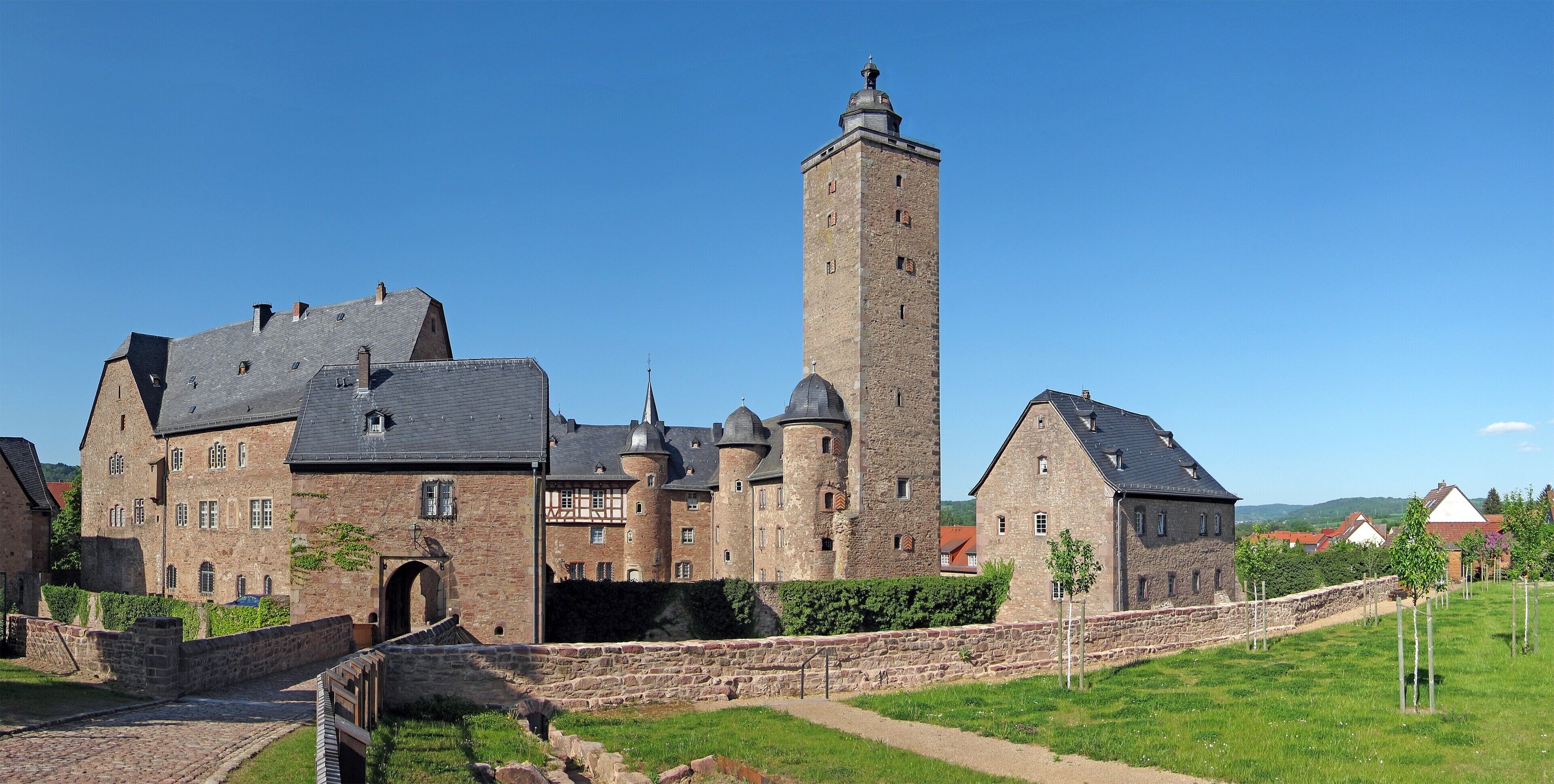 A historic stone building with a prominent tower, a courtyard, and a bridge.