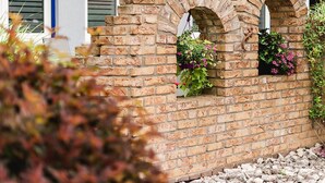 Un muro di mattoni con finestre ad arco e cesti di fiori appesi.