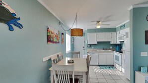 Una cucina con mobili bianchi, un tavolo da pranzo con sedie, una ventola a soffitto e un quadro colorato appeso al muro.