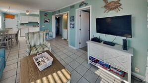 Un soggiorno con televisore, ventilatore a soffitto, zona pranzo con sedie e cucina sullo sfondo.