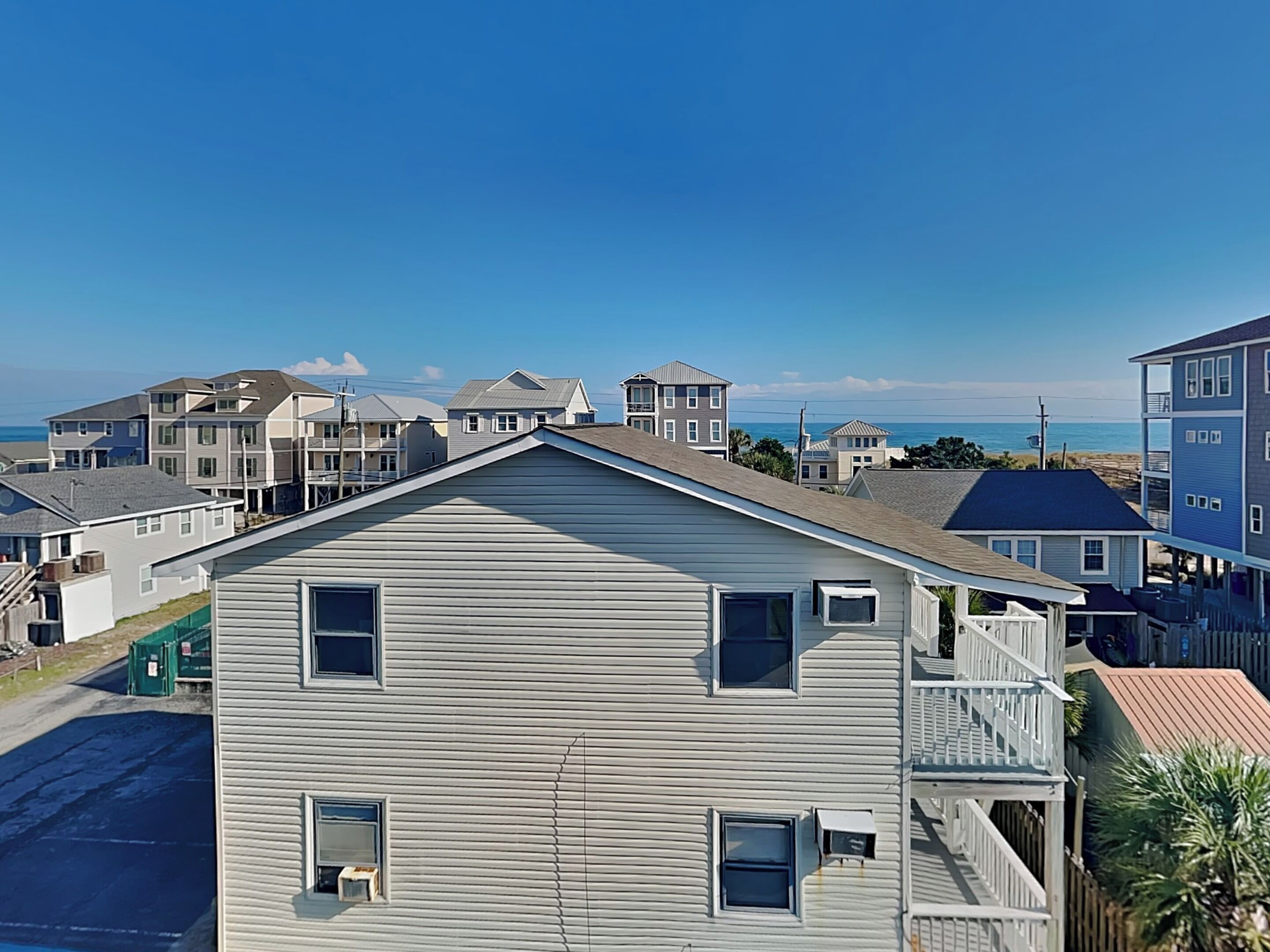 Una zona residencial costera con varias casas de dos pisos, algunas con balcones, y una vista despejada del océano.