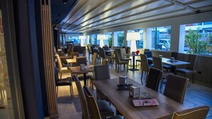 A modern restaurant with multiple tables and chairs, large windows, and a ceiling with linear light fixtures. - HOTEL BUSINESS (Casoria)
