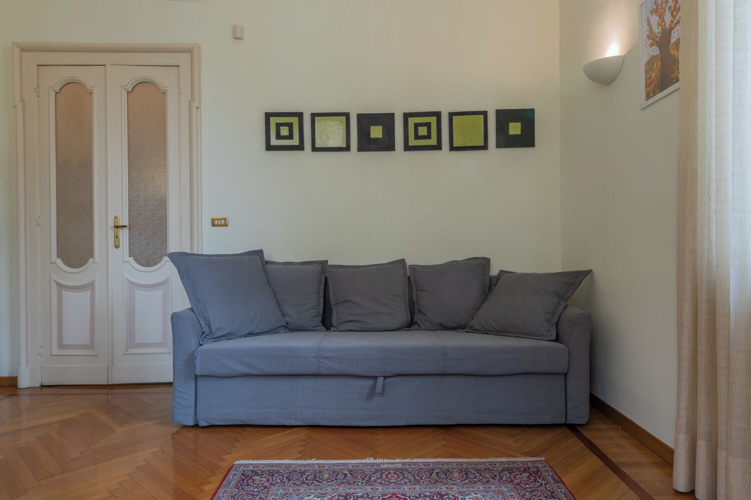 Una sala de estar con un sofá gris, un tapete estampado y una pared con obras de arte cuadradas enmarcadas.