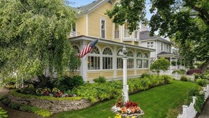 Een huis met twee verdiepingen, een veranda, een stenen steunmuur en een verzorgde tuin met verschillende planten en bloemen.