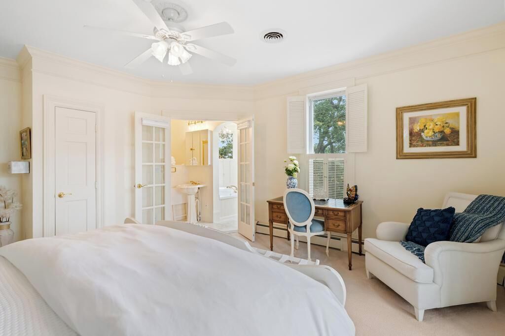 A bedroom with a bed, a desk, a chair, a white armchair, and a ceiling fan.