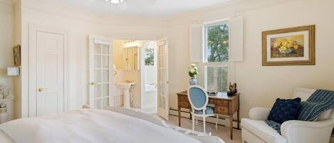 A bedroom with a bed, a desk, a chair, a white armchair, and a ceiling fan.