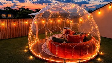 Een transparante koepelstructuur met een rond zitgedeelte van binnen, omringd door lichtjes.