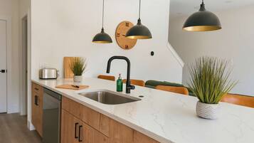 Een moderne keuken met een wit marmeren aanrecht, houten kastjes, een roestvrijstalen spoelbak en twee hanglampen.