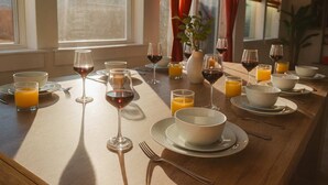 Tavola imbandita per la colazione, con bicchieri da vino, succo d'arancia e ciotole, affacciata sull'esterno.