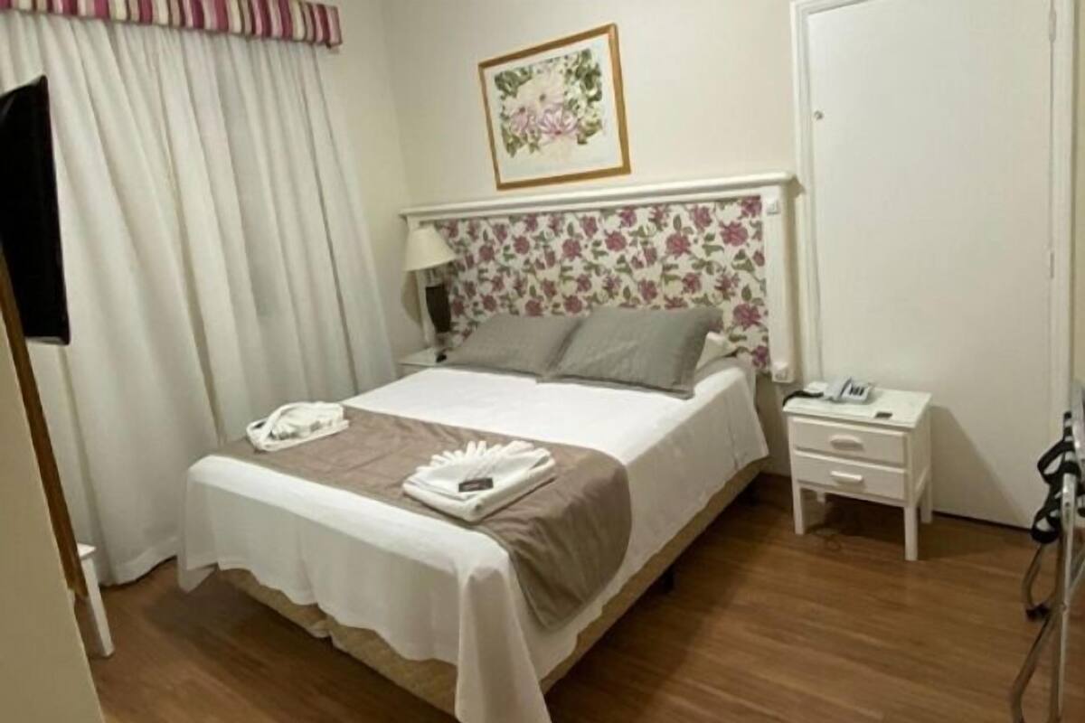 Une chambre d’hôtel avec un lit, une table de chevet avec un téléphone, une commode et un rideau.