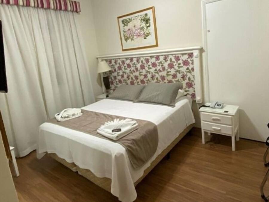 Habitación de hotel con una cama, una mesita de noche con teléfono, una mesita auxiliar y una cortina.