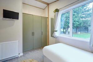 A bedroom with a bed, a window with curtains, a radiator, and a wardrobe. - Host & Stay | Lucky Lodge (Pocklington)