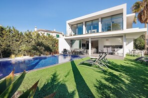 Una casa moderna con piscina, mobiliario exterior y abundante vegetación.