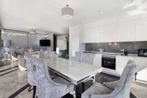 Una cocina moderna con armarios blancos, un comedor con mesa de mármol y una sala de estar con sofá y televisión.