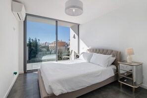 Un dormitorio con una cama grande, una mesita de noche, una lámpara y un ventanal corredero que da a un balcón.