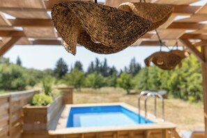 Een houten pergola met hangende gevlochten manden en een zwembad.