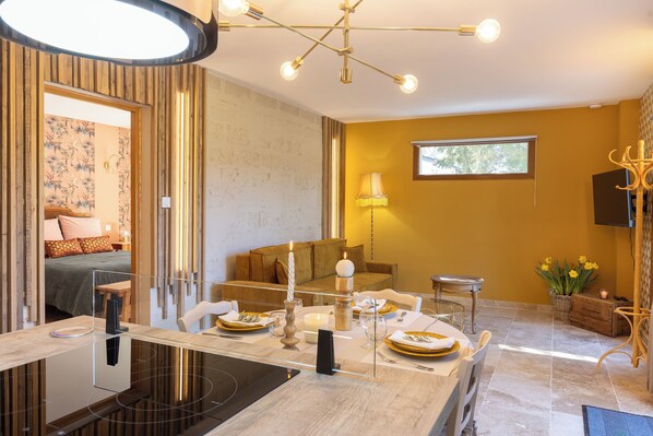 Een moderne eetruimte met een glazen tafel, een kaarsen decoratie en uitzicht op een slaapkamer met een bed en gordijnen.