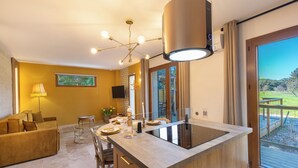 A modern kitchen with a central island, a dining area with a sofa, and a large sliding glass door leading to an outdoor deck. - Mas9Romanin:Gîte Evasion in Provence (Saint-Rémy-de-Provence)