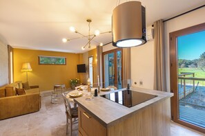 A modern kitchen with a central island, a dining area with a sofa, and a large sliding glass door leading to an outdoor deck. - Mas9Romanin:Gîte Evasion in Provence (Saint-Rémy-de-Provence)