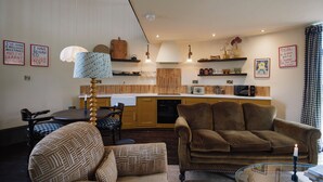 A cozy living room with a brown sofa and patterned armchair, a glass coffee table, and a dining area with a checkered tablecloth.