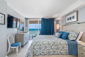 A bedroom with a large bed, a dresser, a chair, and a view of the sea through a balcony door. - 🌞2 Beachfront Condos Side by Side🌴Sand Castle II 2601/2602🐬 Pool/Hot Tub (Indian Shores)