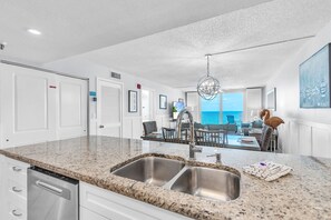 A modern kitchen with granite countertops, stainless steel sinks, and a dishwasher. - 🌞2 Beachfront Condos Side by Side🌴Sand Castle II 2601/2602🐬 Pool/Hot Tub (Indian Shores)