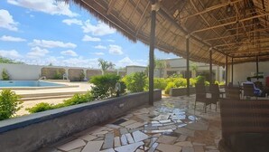 An outdoor patio with stone flooring, wicker furniture, and a pool in the background.