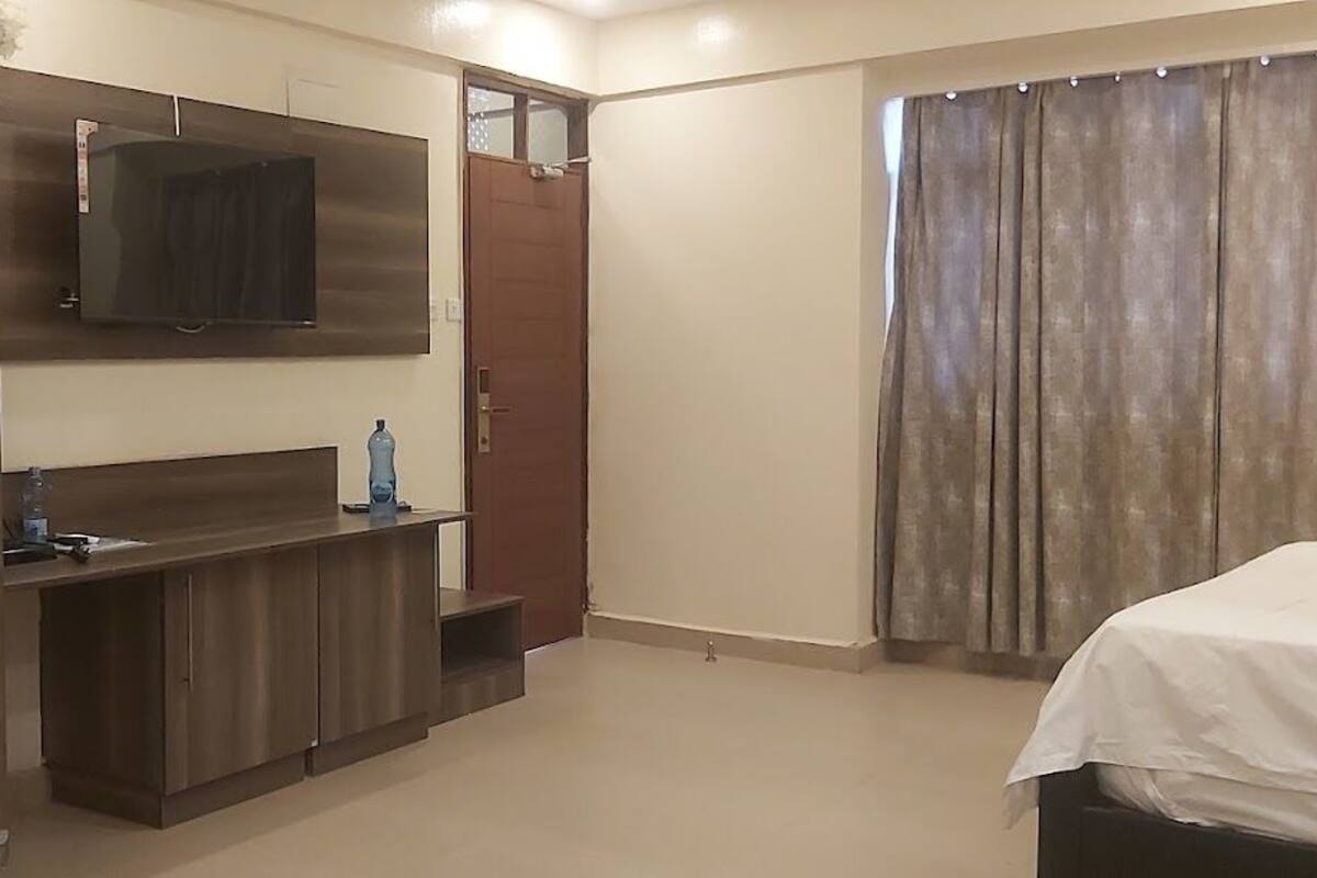 Ein Schlafzimmer mit Bett, einem an der Wand befestigten Fernseher, einem Kleiderschrank und einem Vorhang.